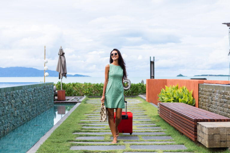 happy-caucasian-pretty-long-hair-elegant-tourist-woman-dress-with-red-suitcase-outside-hotel